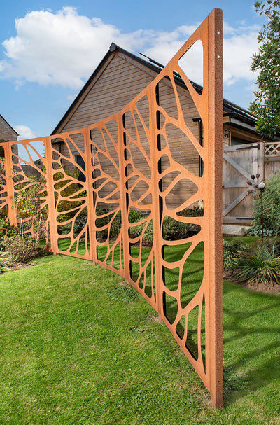 Decorative metal fence with intricate cut-out design in a garden setting.